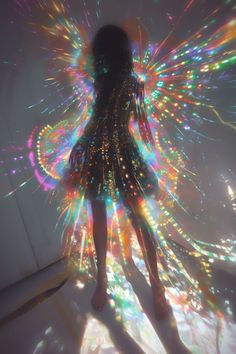 a woman standing in the middle of a room with colorful lights on her body and wings