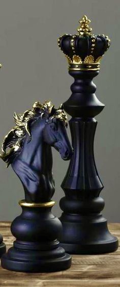 two black and gold chess pieces sitting on top of a wooden table next to each other