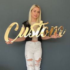 a woman holding up the word custom in gold foil on a grey background with ripped jeans