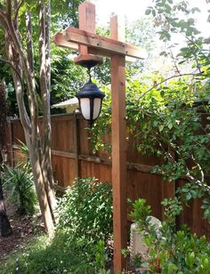 a lamp hanging from the side of a wooden structure in a garden with trees and bushes