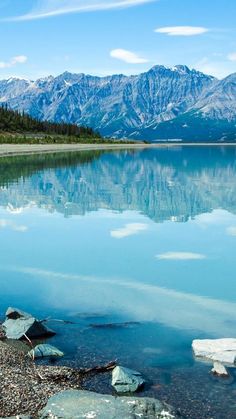 a lake with mountains in the background and rocks on the ground near it's edge