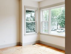 an empty room with wooden floors and two windows in the corner, looking out onto a parking lot