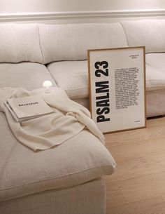 a white couch sitting on top of a hard wood floor next to a framed poster