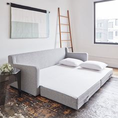 a couch with pillows on it in front of a window and a ladder leaning against the wall