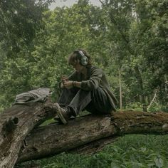 a woman sitting on top of a tree branch in the forest with headphones on