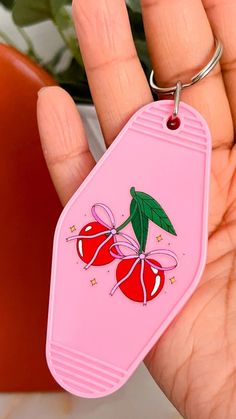 a pink keychain with cherries on it is held in someone's hand