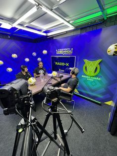 three men sitting at a table in front of microphones with balls on the wall behind them