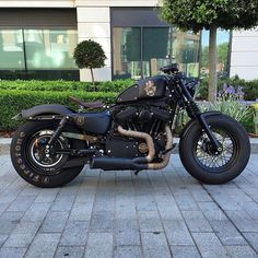 a black motorcycle parked on the sidewalk in front of a building with plants and bushes