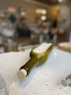 a green bottle sitting on top of a white counter next to a wine glass filled with liquid