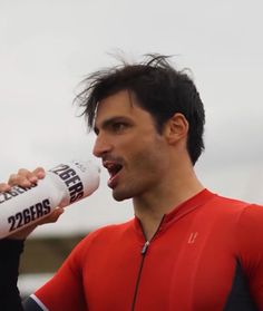 a man in a red shirt drinking from a water bottle with his mouth wide open