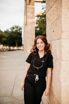 a woman standing next to a stone wall with her hands on her hips and smiling at the camera