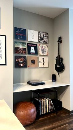 a room with a desk, guitar and various records on the wall