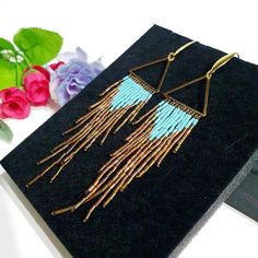 a pair of gold and blue earrings sitting on top of a black box next to flowers