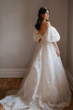 a woman in a white wedding dress standing against a wall with her back to the camera