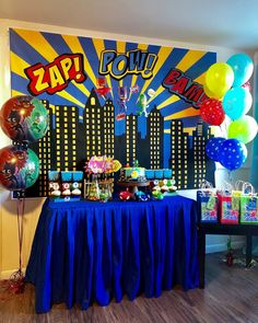 a blue table topped with lots of balloons next to a wall covered in comic books