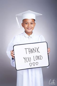 a young boy wearing a graduation cap and gown holding a sign that says thank you lord