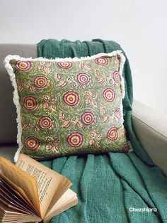 an open book sitting on top of a green couch next to a pillow and blanket