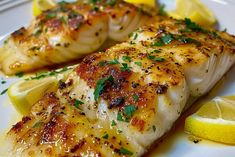 two fish fillets on a white plate with lemon wedges