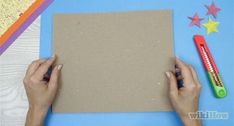 two hands holding a piece of cardboard on top of crafting supplies