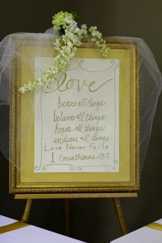 a framed sign with flowers on it sitting next to a white table cloth covered chair