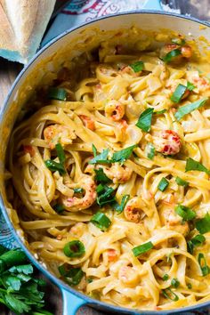 pasta with shrimp and parsley in a blue pot on a wooden table next to bread