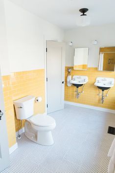 a bathroom with yellow and white tiles on the walls, two sinks and a toilet