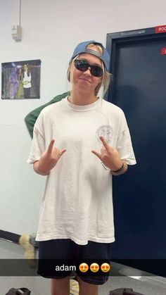 a woman wearing sunglasses and a hat standing in front of a door with her hands up