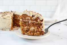 a slice of carrot cake with cream cheese frosting on a plate next to a fork