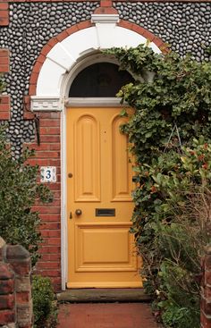 a yellow door is in front of a brick building with ivy growing on the side