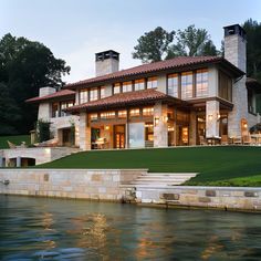 a large house sitting on top of a lake next to a lush green hillside covered in trees