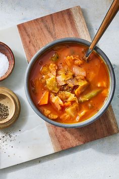 a bowl of soup on a cutting board next to two bowls of salt and pepper