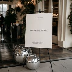 a welcome sign sitting next to two shiny balls on the floor in front of a building