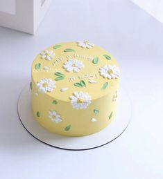 a yellow cake with white flowers on it sitting on top of a table next to a box