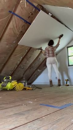 a woman standing on top of a wooden floor in a room with unfinished walls and beams