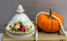 an orange pumpkin sitting on top of a book next to a tea pot and saucer