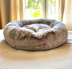 a round dog bed on top of a bed in front of a window with curtains