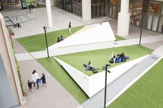 people are sitting on the grass in front of a large triangular shaped building with green roof