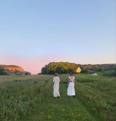 two women in white dresses walking through a field