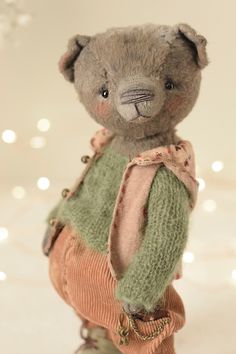 a teddy bear dressed in sweaters and pants on a white surface with lights behind it