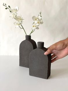 a hand is reaching for two vases with flowers in them on a white surface