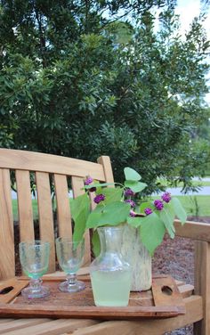 a wooden bench sitting next to a vase with purple flowers in it on top of a table