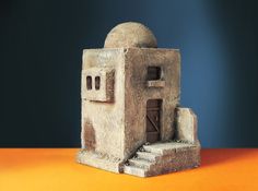 a small stone building sitting on top of an orange table next to a blue wall