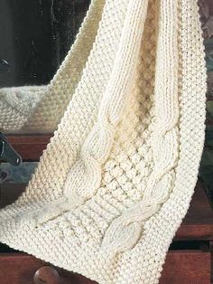 a white knitted blanket sitting on top of a wooden table next to a mirror