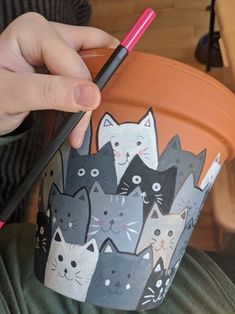 a person holding a pencil in their hand while painting a pot with cats on it