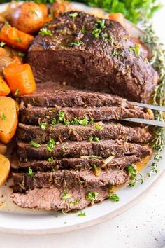 a white plate topped with meat and veggies next to carrots on a table