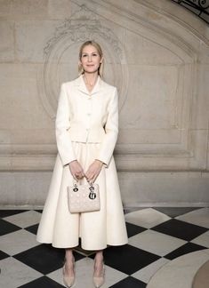 a woman standing in front of a marble wall holding a white purse and posing for the camera