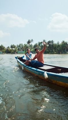 two people in a small boat on the water with palm trees and blue sky behind them