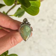 Truly beautiful Silver Peak Variscite teardrop along with a teardrop Madagascar Sapphire in similar green and gold tones. Both stones are wrapped in fine silver with sterling silver embellishments and band. Sits on a simple rectangular sterling silver band. Size 9 All of my work is hand crafted, from sourcing the stones from sustainable miners and lapidary artist, to forging the piece from sterling and fine silver sheet metal and wire. Over time, sterling silver develops a lovely patina, the mor Silver Teardrop Emerald Ring Gift, Silver Teardrop Ring With Gemstone Accents, Teardrop Chrysoprase Gemstone Jewelry, Sterling Silver Multi-stone Teardrop Ring, Green Teardrop Gemstone Accents Jewelry, Green Pear-shaped Sterling Silver Jewelry, Green Teardrop Gemstone Jewelry, Green Teardrop Jewelry With Gemstone Accents, Green Teardrop Nature-inspired Jewelry