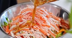 someone pouring dressing onto a salad in a silver bowl on top of a white table