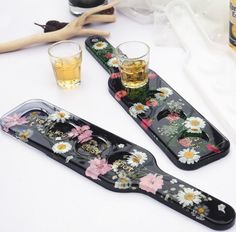 two glasses sitting on top of trays next to bottles and spoons with flowers painted on them